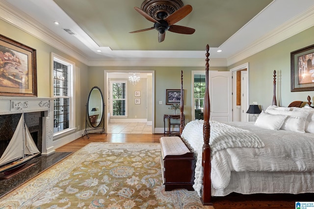 bedroom with ornamental molding, a high end fireplace, ceiling fan with notable chandelier, and light hardwood / wood-style flooring