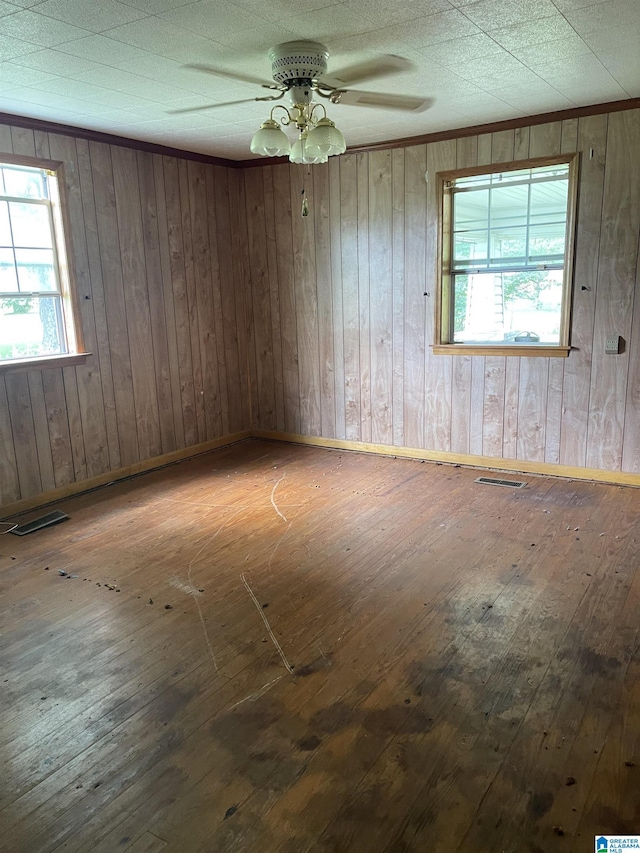 spare room with ceiling fan, wood-type flooring, and wooden walls