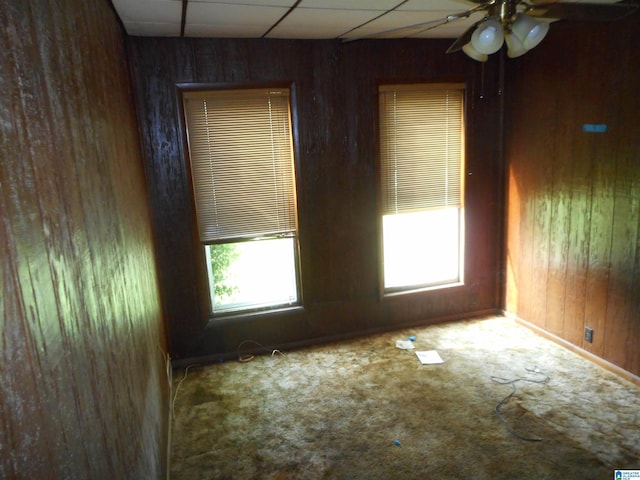 empty room with a ceiling fan, a paneled ceiling, carpet flooring, and wooden walls