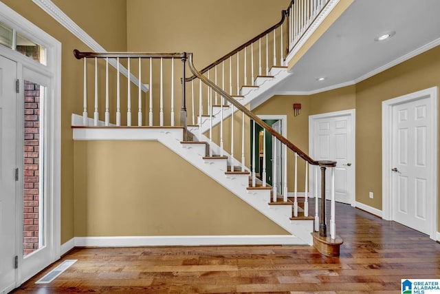 stairway featuring crown molding, wood-type flooring, and a towering ceiling