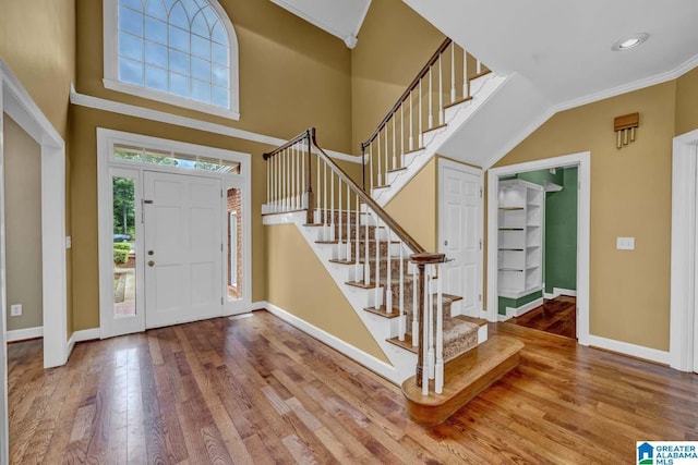 foyer with wood-type flooring, a towering ceiling, and crown molding