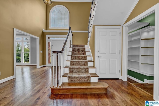 entryway featuring ornamental molding, a towering ceiling, and hardwood / wood-style floors