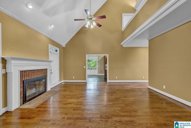 unfurnished living room featuring crown molding, high vaulted ceiling, a brick fireplace, hardwood / wood-style flooring, and ceiling fan