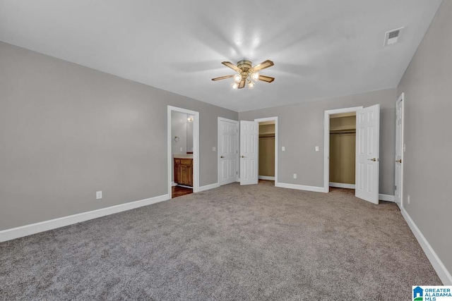 unfurnished bedroom featuring two closets, carpet floors, ensuite bath, and ceiling fan