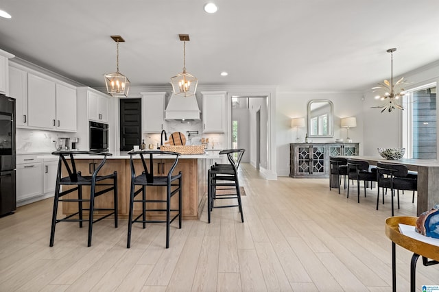 kitchen featuring pendant lighting, white cabinetry, black appliances, and an island with sink