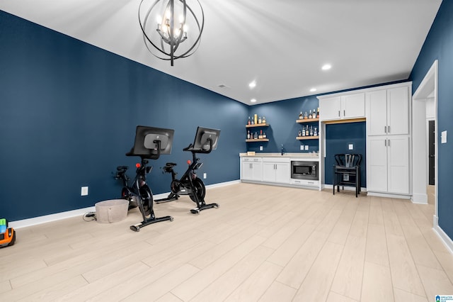 exercise area with a notable chandelier, wet bar, and light wood-type flooring