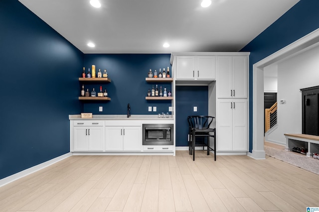 bar featuring stainless steel microwave, white cabinets, and light hardwood / wood-style flooring