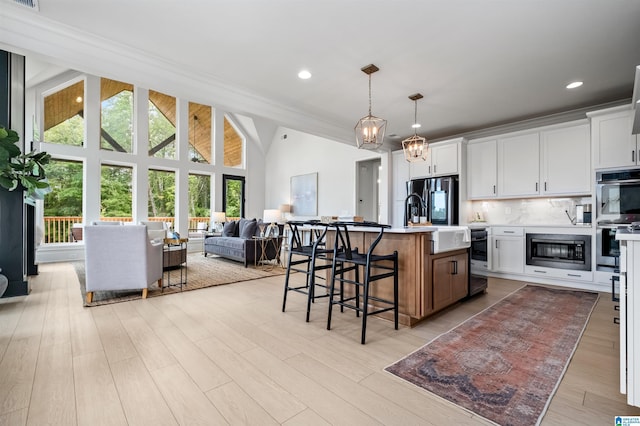 kitchen featuring pendant lighting, a kitchen island with sink, white cabinets, built in microwave, and black fridge with ice dispenser