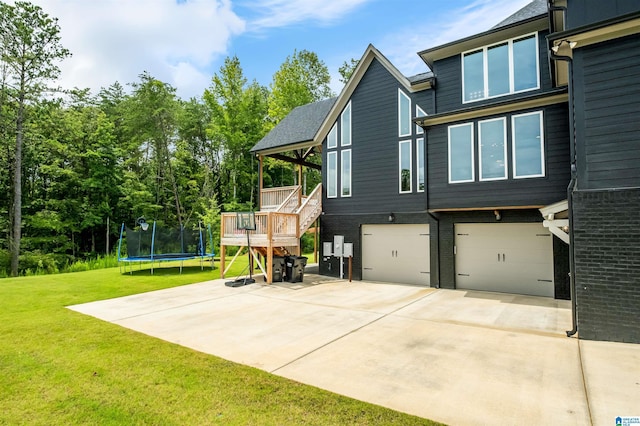 exterior space with a trampoline, a wooden deck, a garage, and a lawn