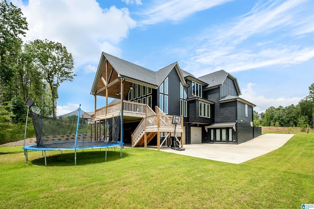 rear view of property featuring a trampoline, a yard, a patio area, and a deck