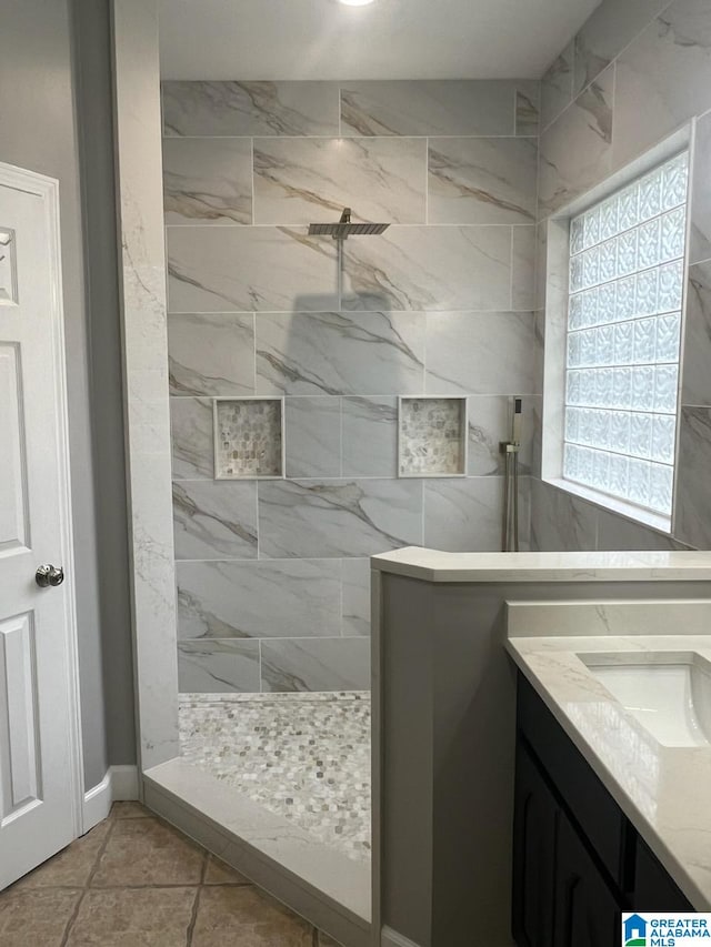 bathroom with a tile shower, vanity, and tile patterned flooring