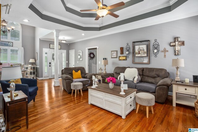 living room featuring crown molding, hardwood / wood-style floors, decorative columns, a tray ceiling, and ceiling fan with notable chandelier