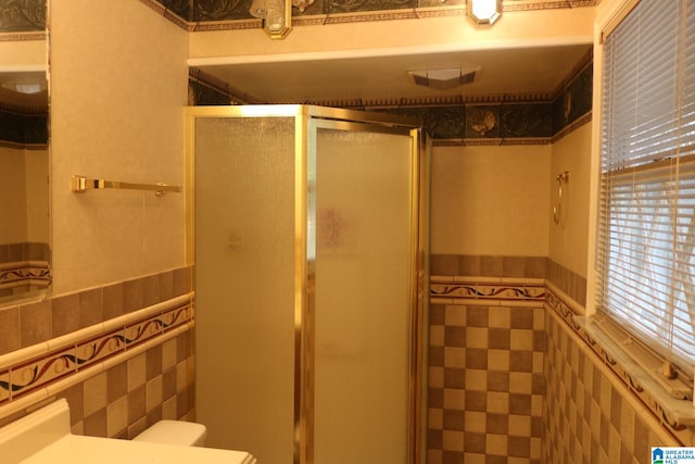 bathroom with a shower with door, toilet, and tile walls