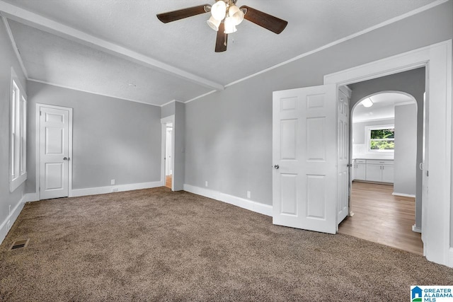 spare room featuring a textured ceiling, carpet floors, ceiling fan, ornamental molding, and beamed ceiling