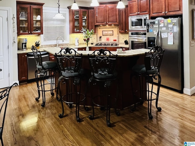 kitchen featuring appliances with stainless steel finishes, backsplash, pendant lighting, and wood-type flooring