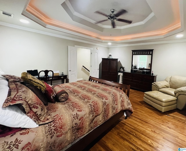 bedroom with hardwood / wood-style floors, ceiling fan, crown molding, and a tray ceiling