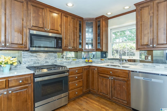 kitchen with stainless steel appliances, brown cabinetry, a sink, and light stone counters