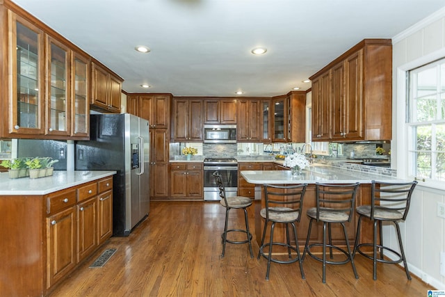 kitchen featuring stainless steel appliances, a breakfast bar, brown cabinetry, and glass insert cabinets