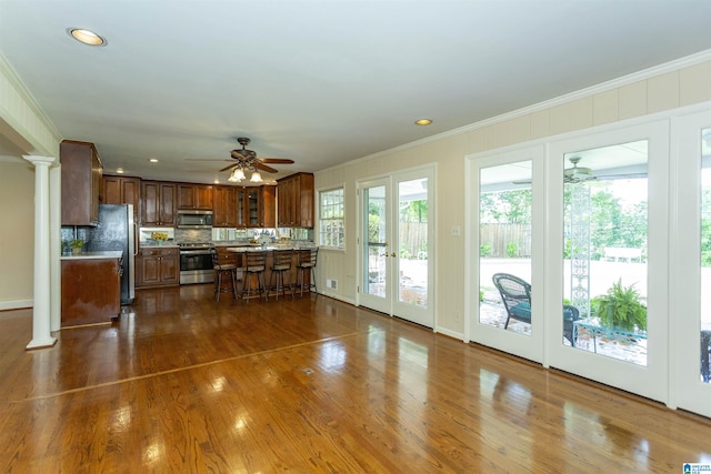 kitchen featuring dark wood-style floors, brown cabinets, decorative columns, crown molding, and appliances with stainless steel finishes