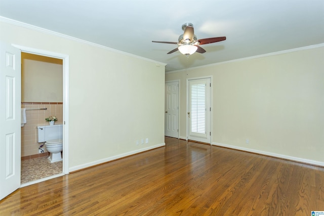 unfurnished bedroom featuring ceiling fan, ornamental molding, wood finished floors, ensuite bathroom, and tile walls