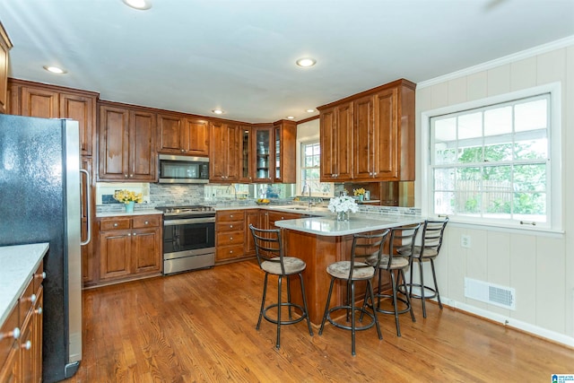 kitchen with appliances with stainless steel finishes, a healthy amount of sunlight, hardwood / wood-style flooring, and a kitchen bar