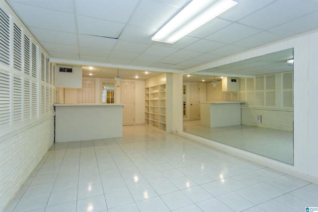 unfurnished room with a paneled ceiling, light tile patterned floors, brick wall, and visible vents