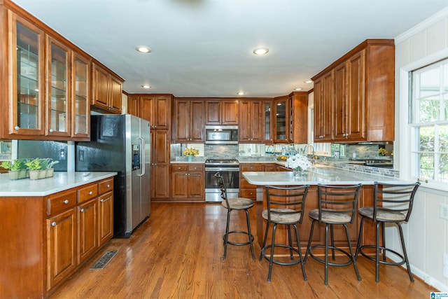 kitchen featuring kitchen peninsula, backsplash, a kitchen bar, wood-type flooring, and appliances with stainless steel finishes