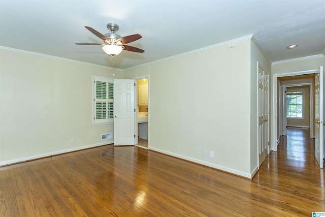 empty room featuring visible vents, crown molding, baseboards, and wood finished floors