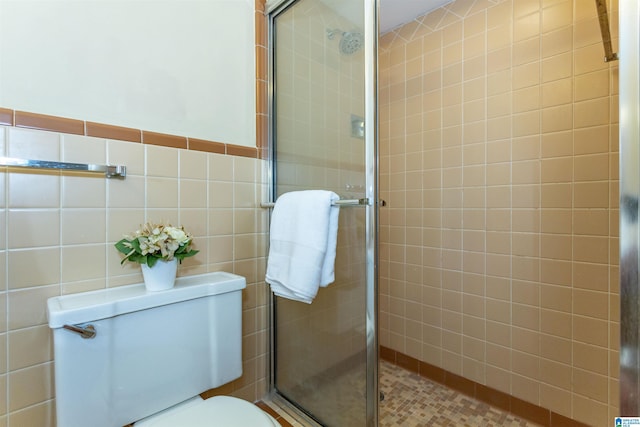 bathroom with toilet, a wainscoted wall, a tile shower, and tile walls