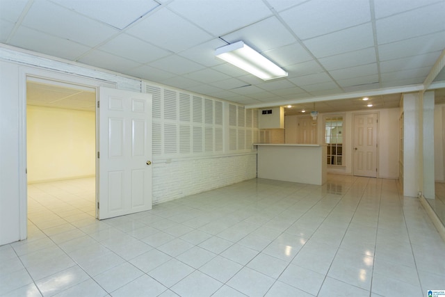 empty room with light tile patterned floors, brick wall, and a paneled ceiling