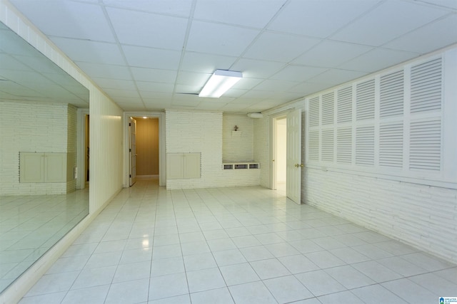 spare room featuring light tile patterned floors, brick wall, and a drop ceiling