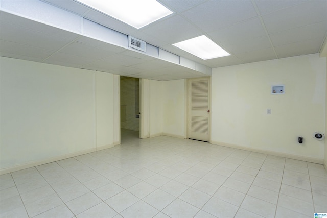 finished below grade area featuring a paneled ceiling, visible vents, baseboards, and light tile patterned flooring