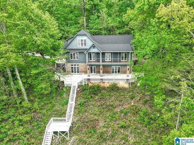 view of front of home featuring a shingled roof, stairway, and a wooded view