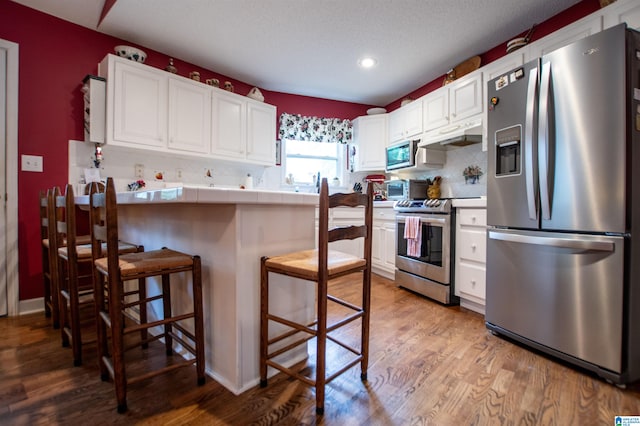 kitchen with stainless steel appliances, light wood-type flooring, white cabinetry, and tile counters