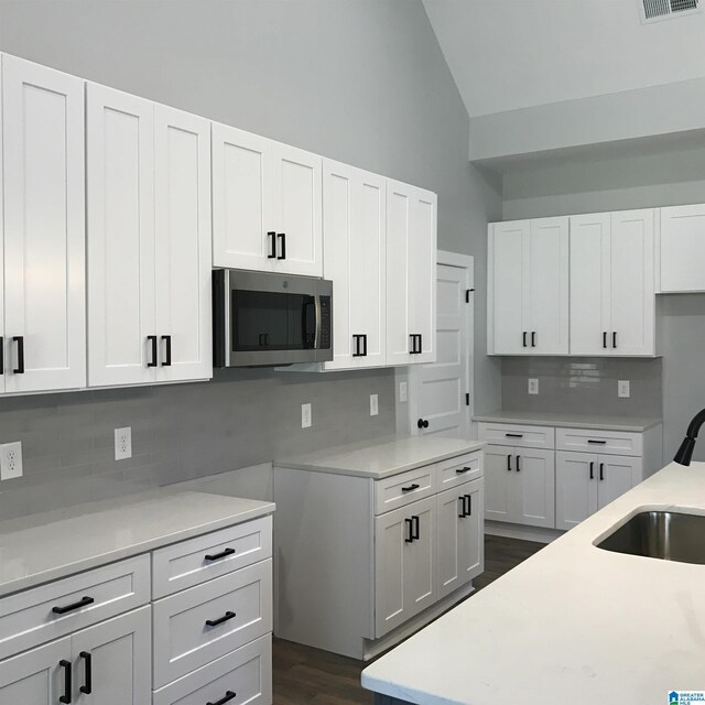 kitchen with tasteful backsplash, white cabinets, vaulted ceiling, and sink