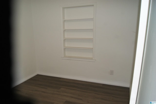 empty room featuring built in shelves and dark hardwood / wood-style flooring