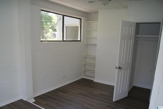 unfurnished bedroom with dark hardwood / wood-style flooring, a closet, and brick wall