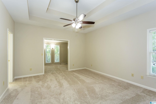 unfurnished room with ceiling fan, light colored carpet, and a tray ceiling