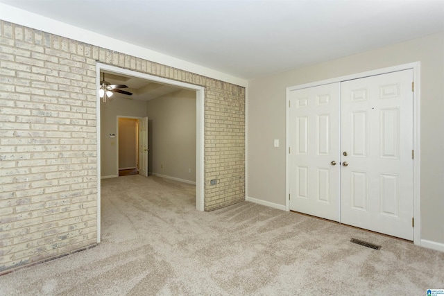 unfurnished bedroom featuring light carpet, a closet, and brick wall