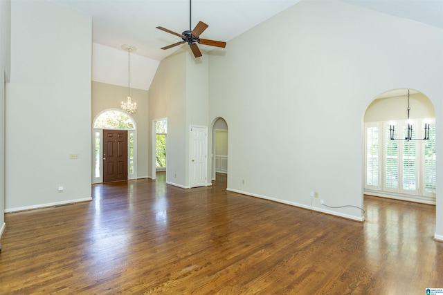 unfurnished living room featuring ceiling fan with notable chandelier, a healthy amount of sunlight, dark wood-type flooring, and high vaulted ceiling