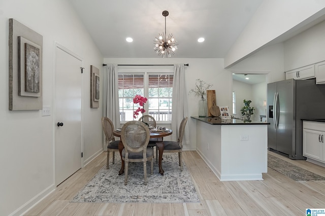 dining area featuring light wood-type flooring, an inviting chandelier, and vaulted ceiling