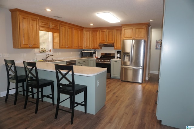 kitchen featuring a kitchen breakfast bar, sink, dark hardwood / wood-style flooring, kitchen peninsula, and stainless steel appliances