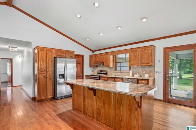 873 Buckelew Rd, Anniston, AL 36207 - kitchen with stainless steel appliances, lofted ceiling, brown cabinetry, a breakfast bar, and light wood-style flooring
