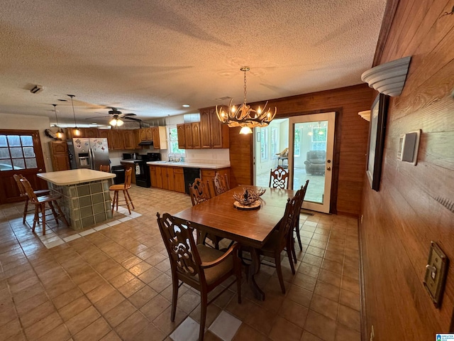 dining space with a textured ceiling, ceiling fan with notable chandelier, wood walls, and sink