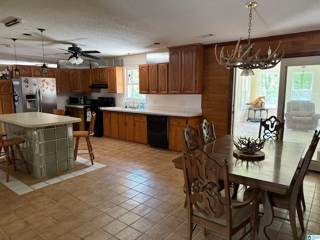 kitchen featuring a kitchen island, a textured ceiling, black appliances, decorative light fixtures, and sink