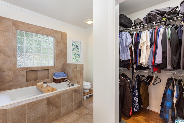 bathroom with a relaxing tiled tub, toilet, and ornamental molding