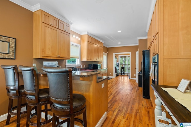 kitchen with ornamental molding, a peninsula, baseboards, a kitchen breakfast bar, and light wood-style flooring