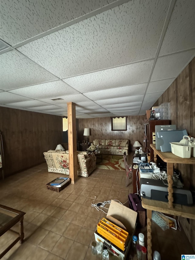 basement featuring wooden walls, tile patterned floors, and a drop ceiling