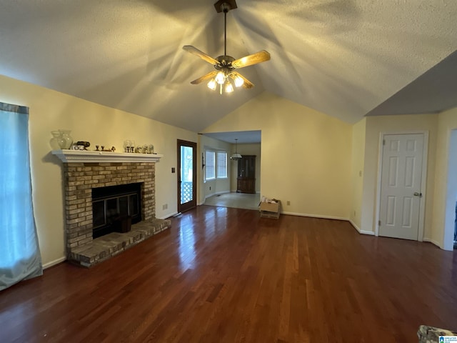 unfurnished living room featuring dark wood-type flooring, a textured ceiling, lofted ceiling, a brick fireplace, and ceiling fan