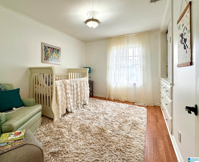 bedroom featuring ornamental molding, a crib, and light wood-type flooring